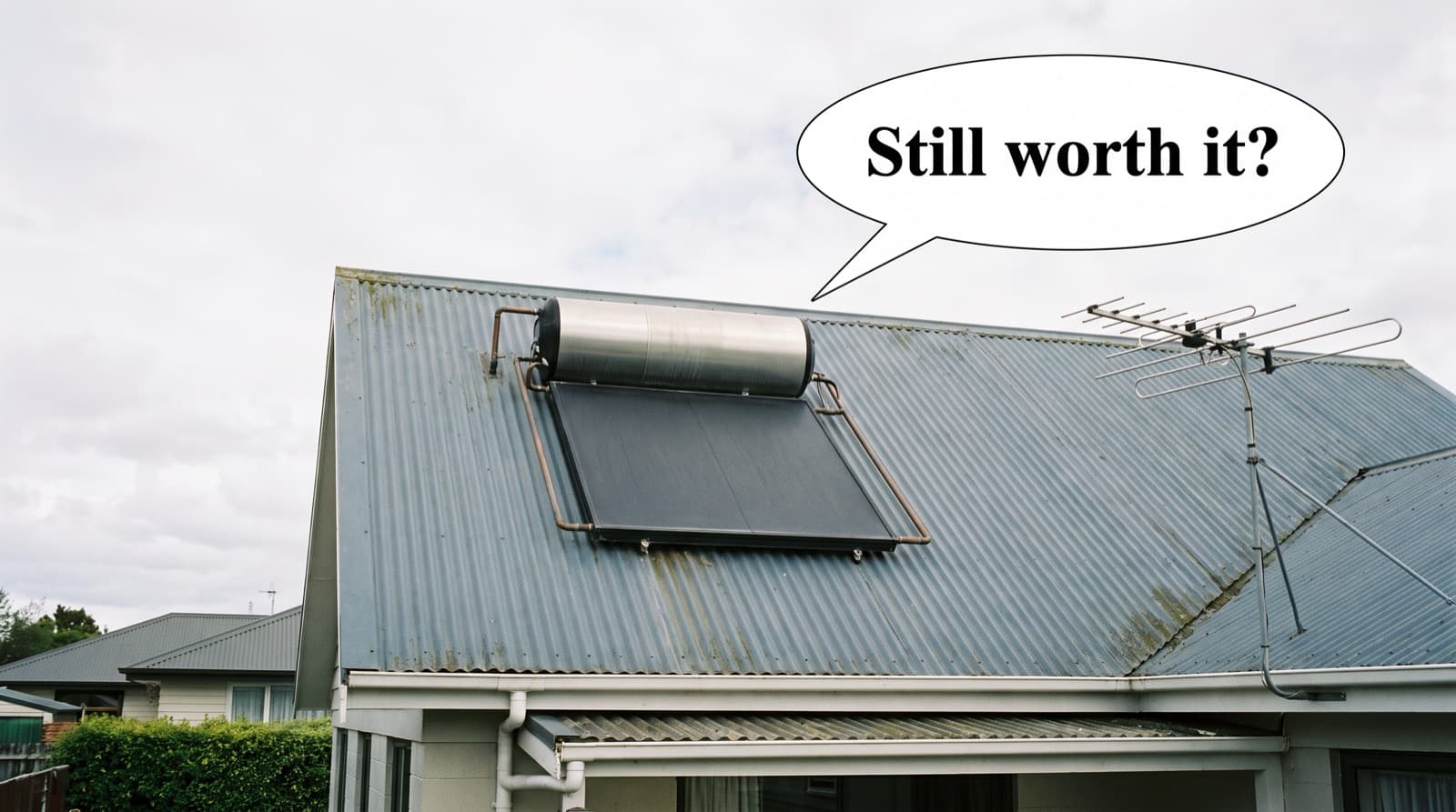 A New Zealand roof with solar water heating panels and a hot water cylinder, speech bubble asking if solar hot water is still worth it