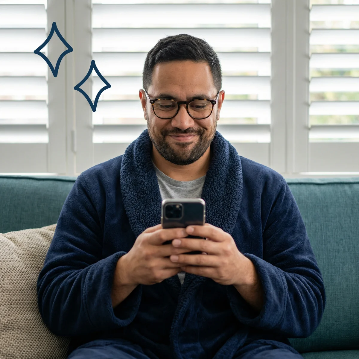 A homeowner in a navy dressing gown smiling at his phone on the sofa